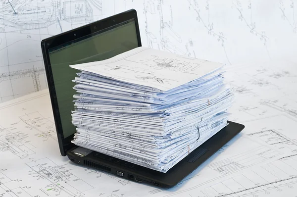 Laptop near pile of project drawings — Stock Photo, Image