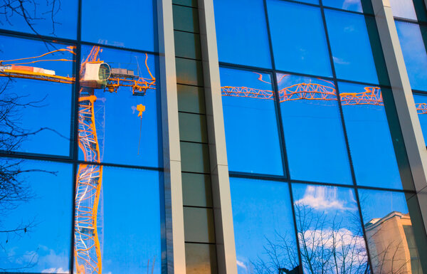 Reflection of a crane in windows of modern office building.