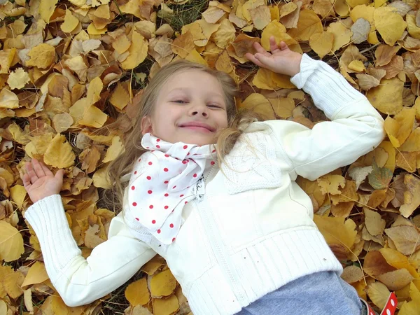 Petite fille allongée sur des feuilles d'automne Photo De Stock