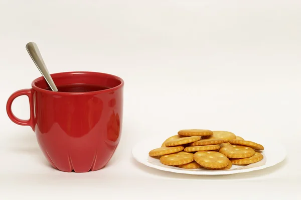 Красная чашка с чаем и тарелкой крекеров — стоковое фото