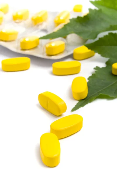 Yellow vitamin pills and green leaves — Stock Photo, Image