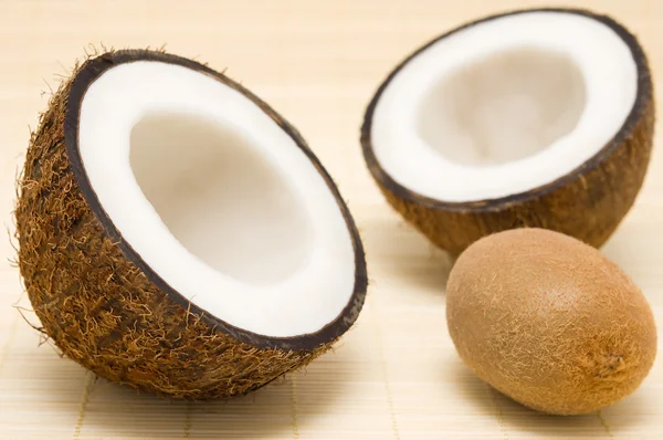 Two halves of coconut, kiwi on a rug. — Stock Photo, Image