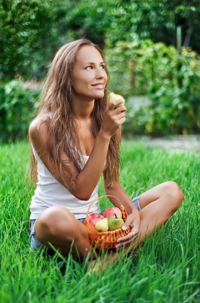 Όμορφη γυναίκα τρώει αχλάδι στο γρασίδι — Φωτογραφία Αρχείου