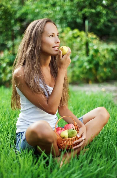 Beautiful lady eating pear on grass — Stock Photo, Image