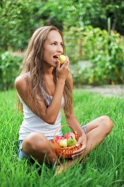 Beautiful woman eating pear on the green — Stock Photo, Image