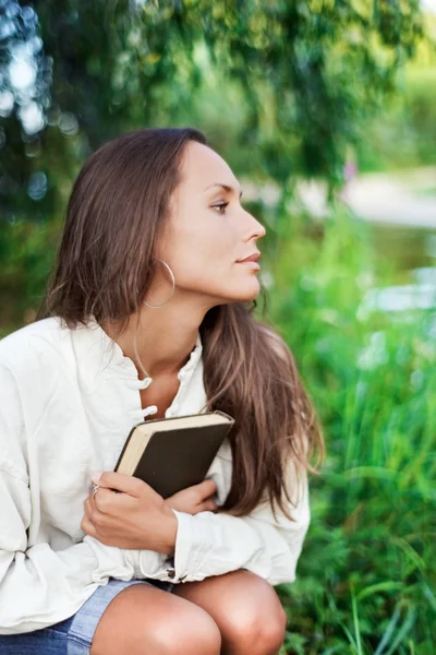 Nachdenkliche junge Frau mit Buch in der Nähe — Stockfoto