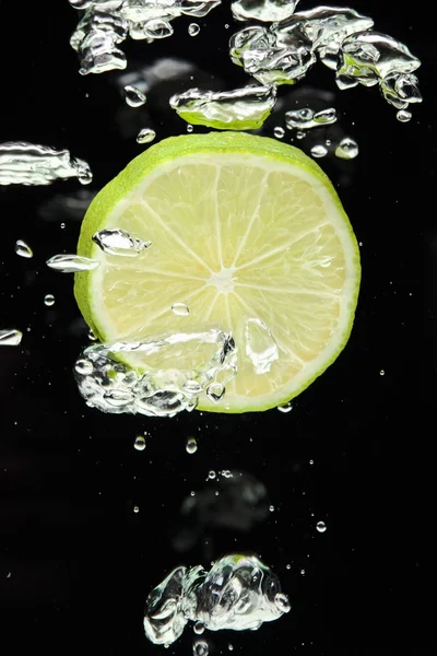 Lima (limón) cayendo en agua sobre negro — Foto de Stock
