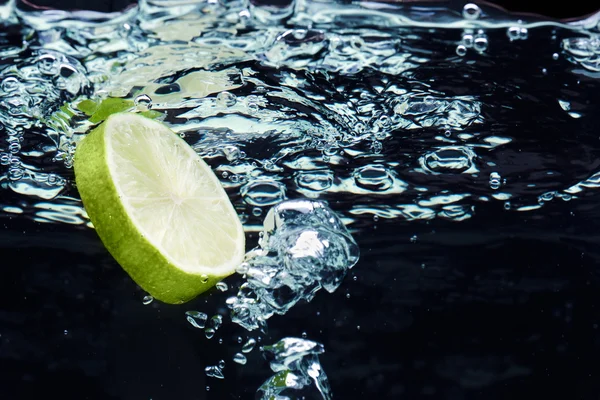 Rebanada de lima (limón) cayendo en agua — Foto de Stock