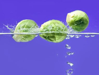 Three Brussels sprouts falling in water clipart