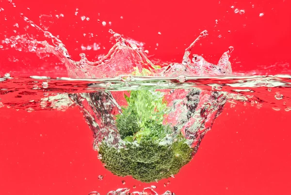Green broccoli falling in water on red — Stock Photo, Image