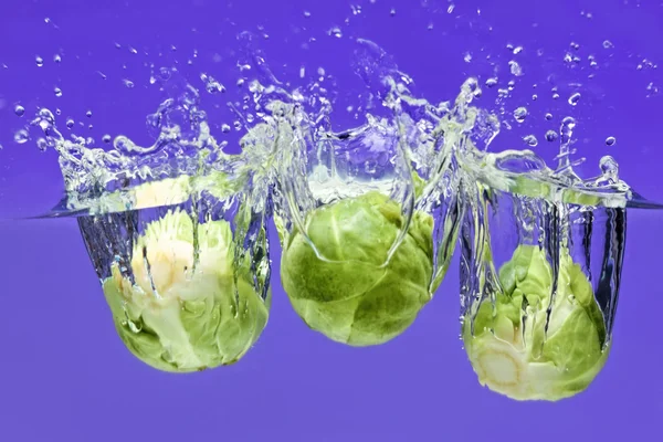 Three Brussels sprouts falling in water — Stock Photo, Image