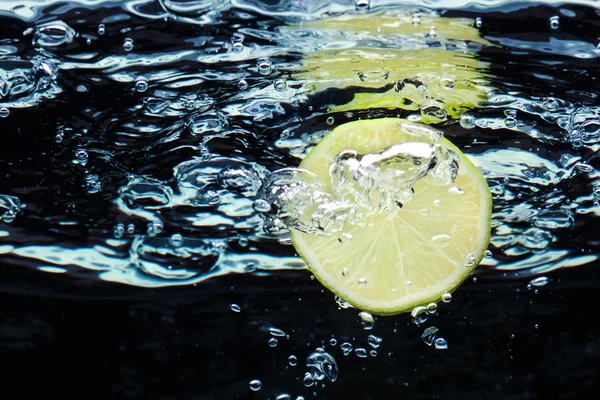 stock image Slice of lime (lemon) falling in water