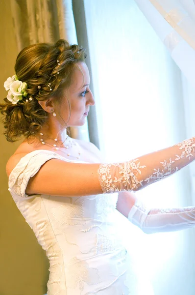 Bruden i en bröllopsklänning mot fönster — Stock fotografie