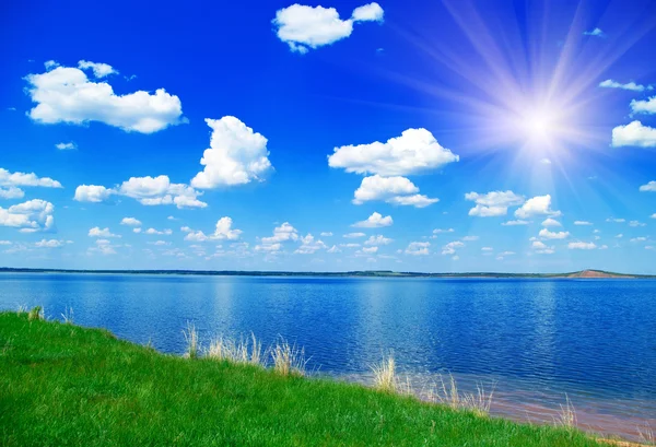 Jezioro, zachmurzone niebo niebieskie i trawa zielona — Zdjęcie stockowe