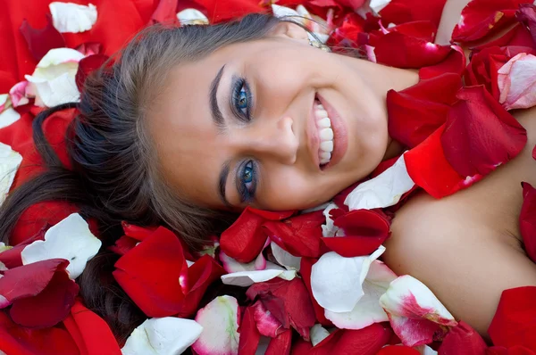 Leende ung flicka i rosenblad — Stockfoto