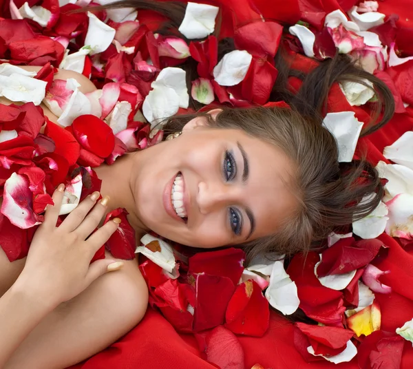 微笑着的年轻女孩，在玫瑰的花瓣 — 图库照片