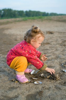 Little girl plays with cockleshells clipart