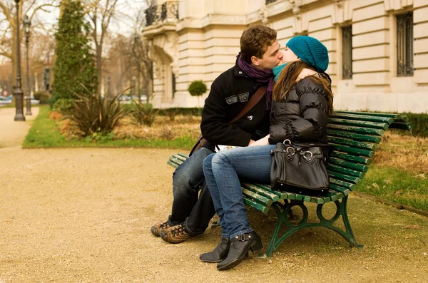 Молодая пара влюблённая целуется на скамейке — стоковое фото