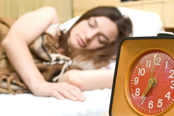 Young woman snoozing a red alarm clock — Stock Photo, Image