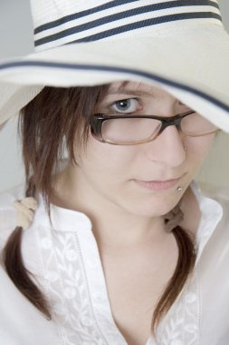 Young girl with glasses looks out from under his hat.