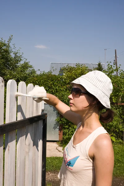Bella ragazza colora una recinzione in legno — Foto Stock