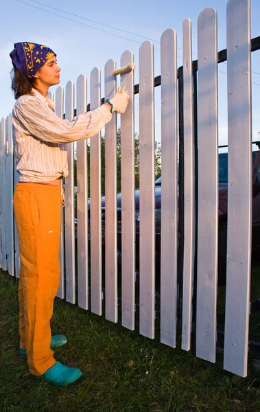 Beautiful girl colours a wooden fence — Stock Photo, Image