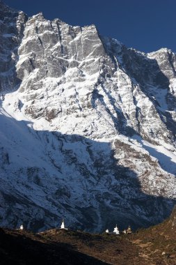 Buddhist stupas dwarfed by mountain cliff, Himalaya, Nepal clipart