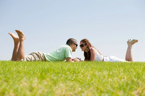 Jovem casal brincalhão que põe em uma grama — Fotografia de Stock