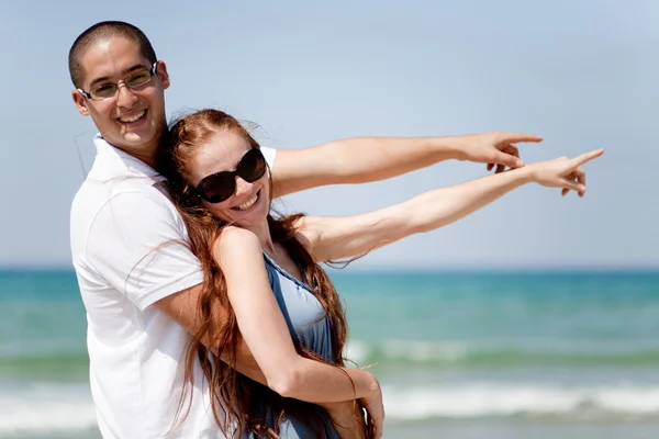 Paar lächelt und zeigt aufs Meer — Stockfoto