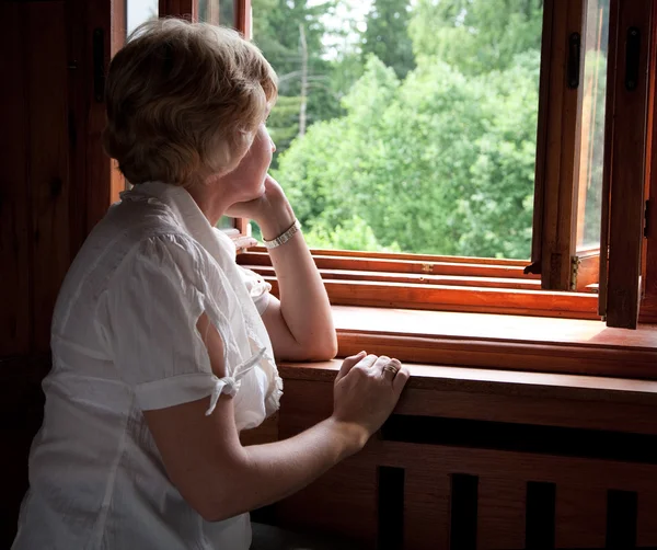 Kobieta patrzy z okna drewniane — Zdjęcie stockowe