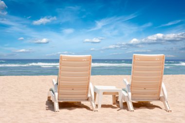 Two chaise longues on beach near ocean clipart