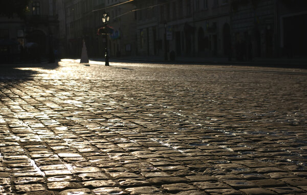 The square of an old European city covered with a wet cobble-stone at the sunrise