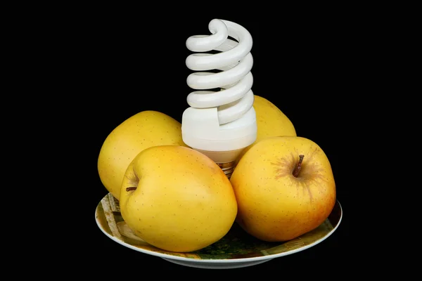 Лампочка и яблоки на тарелке — стоковое фото