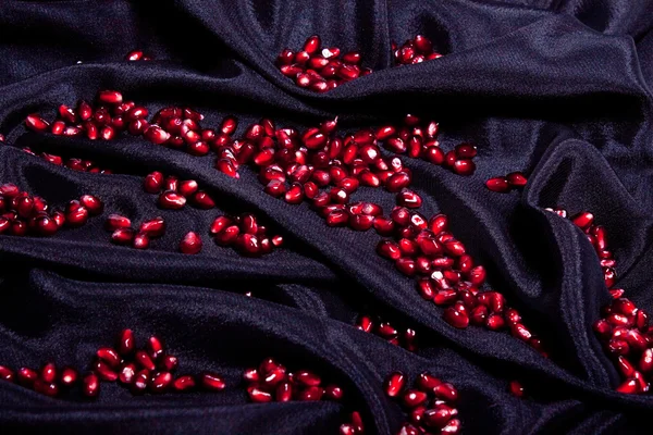 Körner Granatapfel auf schwarzem Seidenstoff. — Stockfoto