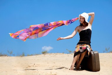 Girl and suitcase standing on the sand clipart