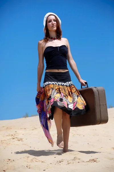 stock image Beautiful girl is walking on a sand with a suitc