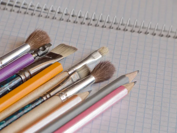 Pencils and brushes on copy-book Royalty Free Stock Photos