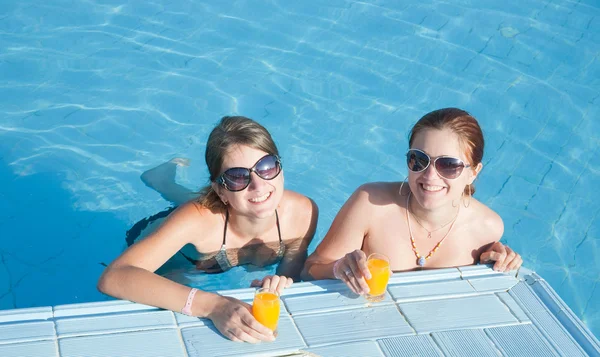 Meninas em piscina tropical com suco de laranja — Fotografia de Stock