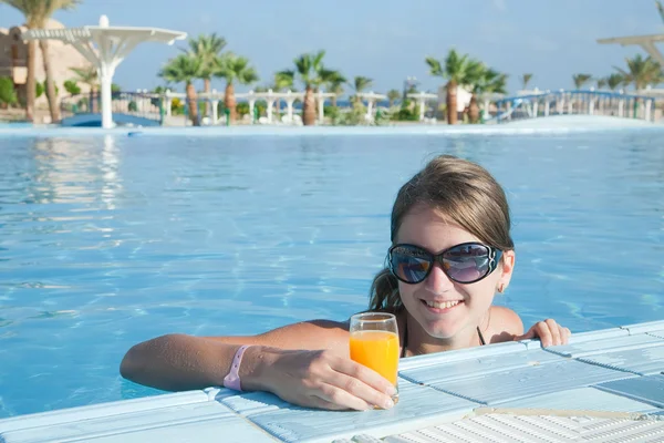 Menina na piscina tropical com suco de laranja — Fotografia de Stock