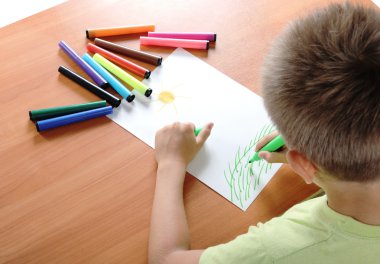 Child draws green grass and sun on white clipart