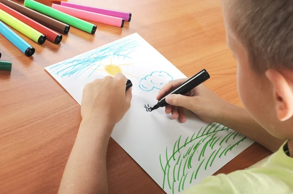 Child draws green grass and sun on paper — Stock Photo, Image
