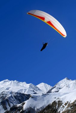 Paraglider flies above mountains clipart