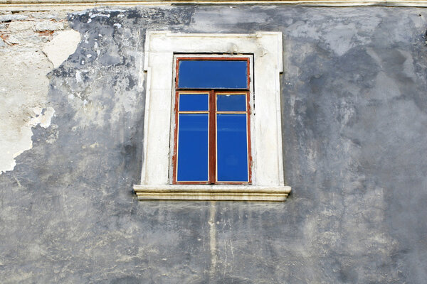 The wall of an old building with a window in which is reflected the blue sky