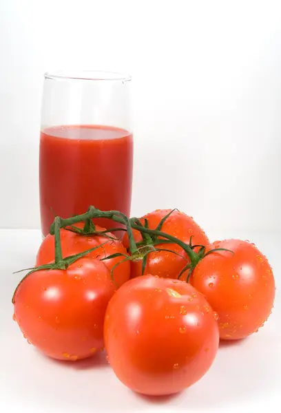 Tomatoes on the vine and glass of juice — Stock Photo, Image