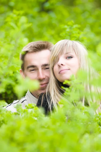 Jovem casal olhar para fora de arbustos verdes — Fotografia de Stock