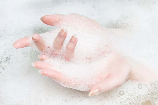Mãos de mulher em um banho com espuma — Fotografia de Stock