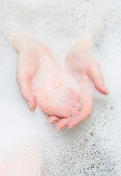Mãos de mulher em um banho com espuma — Fotografia de Stock