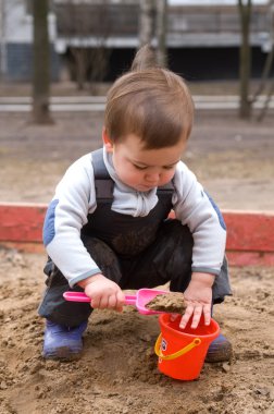 Child sitting in sandbox making mud pie clipart