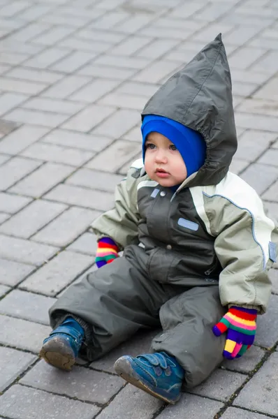 Ένα αγόρι στο πράσινο snowsuit κάθεται στο pavin — Φωτογραφία Αρχείου