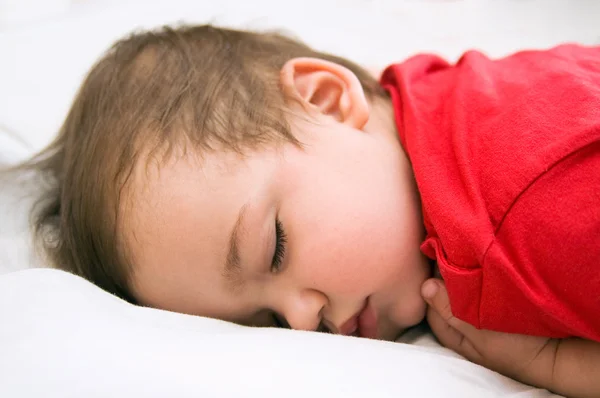 Pojke i röd klänning sova på sängen — Stockfoto